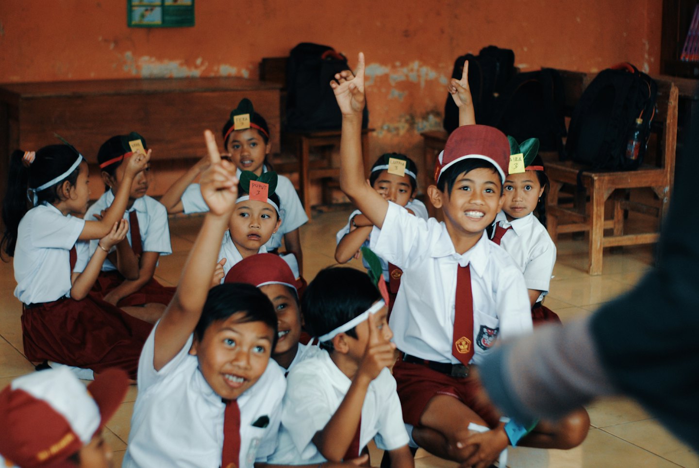 Anak-anak sekolah berseragam merah marun mengangkat tangan di kelas.
