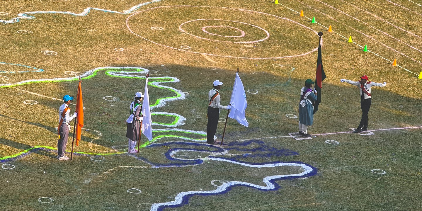 Lima siswa berseragam memegang bendera warna-warni di lapangan berumput.
